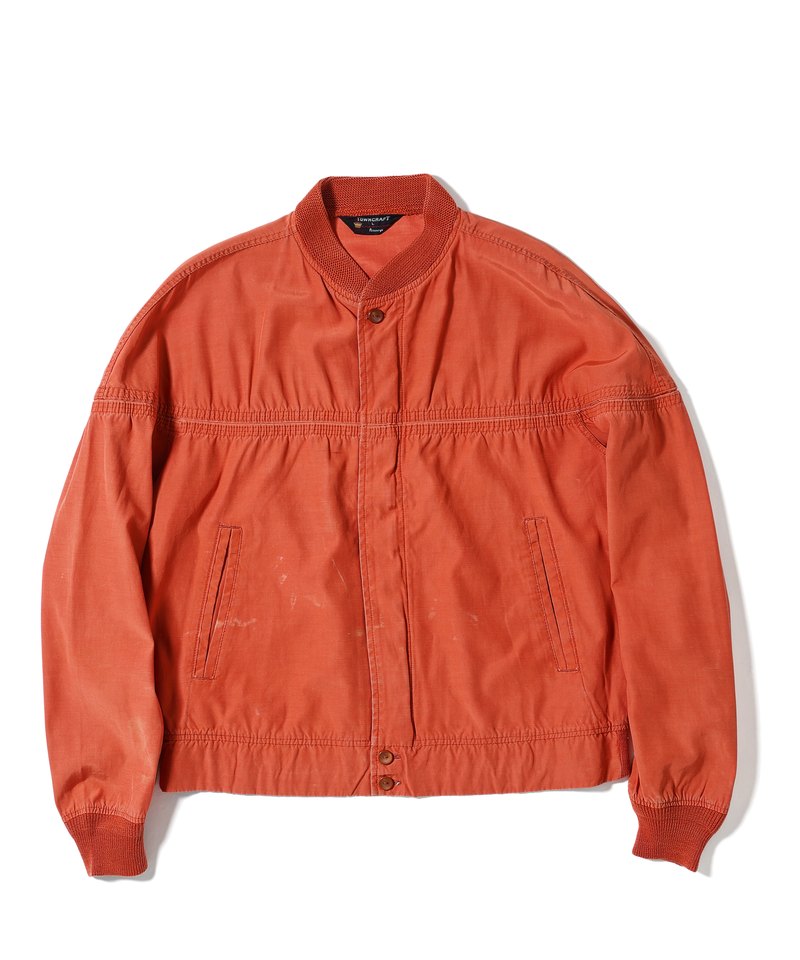 Front of a vintage orange jacket with a rib-knit collar and cuffs, a placket that hides the front zipper with one fastener below the collar and two on the hem band, a seam across the chest and slanted pockets at the waist